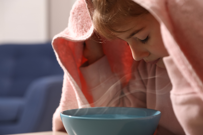 little girl breathing in steam over hot bowl of water